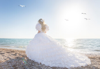Young brunette woman in summer white dress standing on beach and looking to the sea.