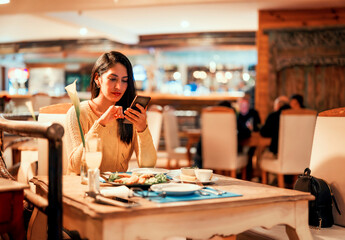 latin young woman sitting alone in a restaurant using smartphone .