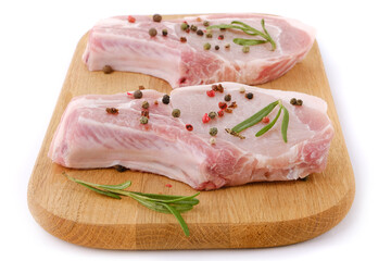Raw pork chops on a cutting board with herbs and spices isolated on white background.