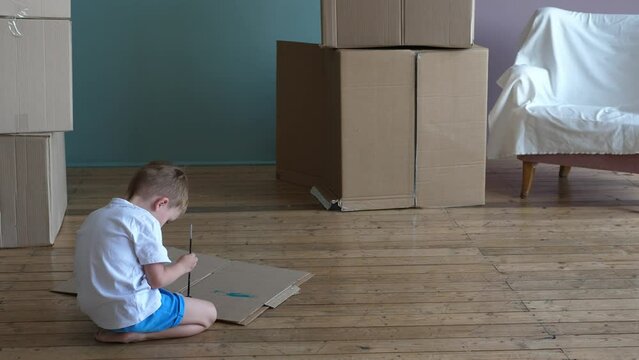 Small happy child paints with watercolor on a cardboard box. A young family moves into a new house