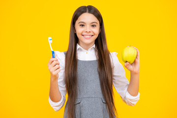 Teenager girl brushing her teeth over isolated yellow background. Apple vitamins for healthy teeth. Daily hygiene teen child hold toothbrush, morning routine. Dental health oral care.