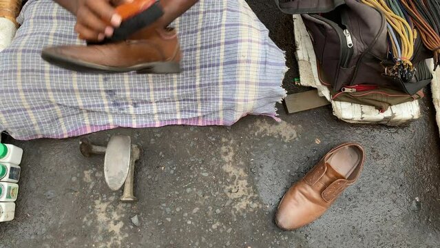 Close up video of a mochee, or poor cobbler, in Kolkata, India, polishing a customer's shoes with black shoe polish
