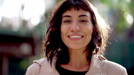 Happy young woman closeup face standing outdoors in sunlight. Portrait of a Brazilian hispanic...