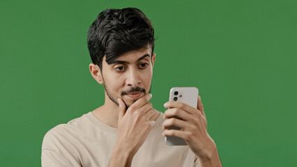 Portrait close-up arabian young man in studio on green background holding phone happy smiling guy browsing social networks make online order read news using modern gadget male customer shopping remote