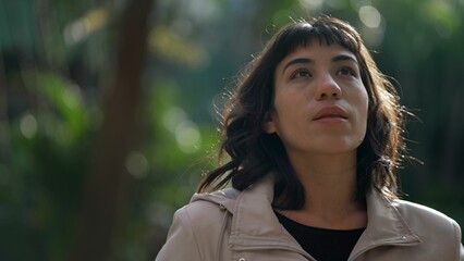 Fototapeta premium South American young woman standing in nature looking at sky. a pensive hispanic girl stands outdoors
