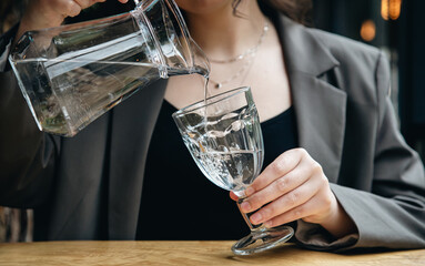 Close-up, a woman pours water into a glass in a cafe.