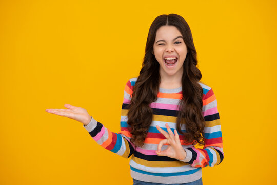Amazed teenager. Portrait of cute teenager child girl pointing hand showing adverts with copy space over yellow background. Excited teen girl.