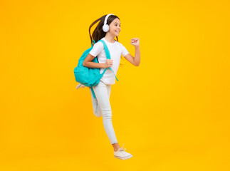 Fototapeta na wymiar School girl, teenager student in headphones on yellow isolated studio background. School and music education concept. Back to school. Jump and run, jumping child.