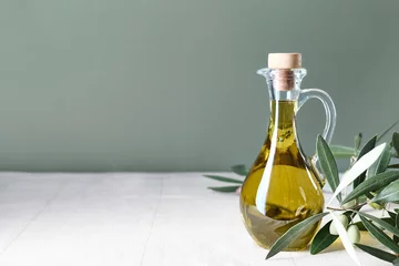Schilderijen op glas Extra virgin olive oil and olive branch in the bottle on the table with linen tablecloth. Healthy mediterranean food. © Caterina Trimarchi