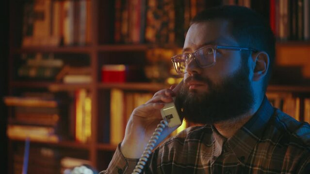 Bearded young man in oldschool eyeglasses talking on vintage corded phone