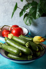Uncooked green zucchinis on a white rustic plate on a blue wooden background.