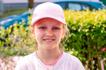 close-up portrait of a little cheerful girl 7-8 years old, in a baseball cap, against the background of a summer landscape