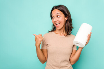 Young hispanic woman holding kitchen roll isolated on blue background points with thumb finger away, laughing and carefree.
