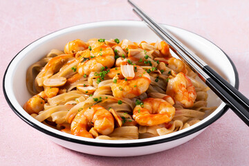 Pad thai with shrimp and peanuts on a pink background.