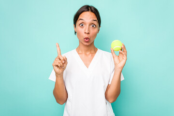 Young hispanic physiotherapy holding a tennis ball isolated on blue background having some great idea, concept of creativity.