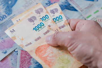 Manos sosteniendo billetes de 1000 pesos argentinos, sobre fondo de billetes azules