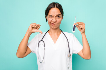 Young hispanic nurse woman holding a thermometer isolated on blue background showing a dislike...