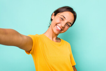 Young hispanic woman doing a selfie isolated on blue background