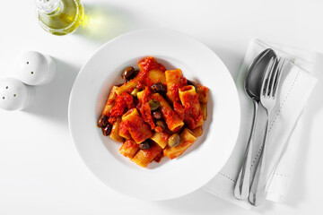 Italian tortiglioni pasta puttanesca with tomato sauce and black olives on the white table serving on the table with cutlery
