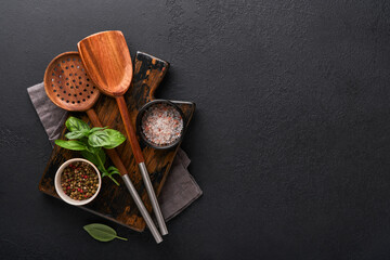 Cooking wooden utensils, basil leaves and spices on dark stone background. Abstract food background. Top view of dark rustic kitchen table with wooden cooking spoon, frame. Banner for your design.