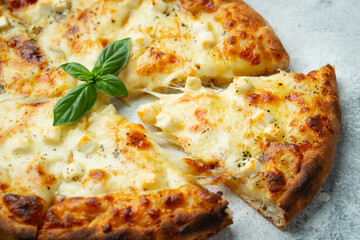 Italian pizza four cheeses with stretching cheese and basil on a light concrete background