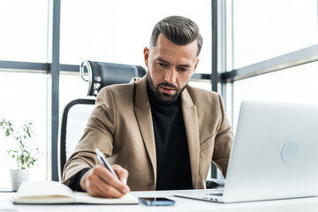 Fototapeta premium A concentrated businessman writes in a notebook sitting in an office