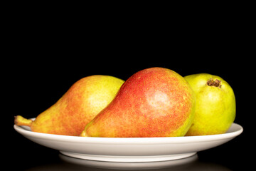 Three organic juicy pears in a white ceramic plate, close-up, isolated on a black background.