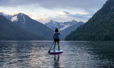 Adventurous Woman Paddle Boarding in a Lake around Canadian Mountain Landscape. Chilliwack Lake, British Columbia, Canada. Adventure Sport Travel