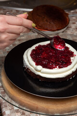 Spreading cherry filling on layer of sponge cake with cream with spoon. Selective focus. Images for articles about cakes, stuffing, confectionery.