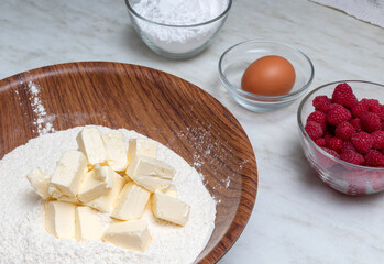 Butter in bowl with flour. On the table are eggs, raspberries, powdered sugar in glass bowls. Selective focus. Image for articles about food, sweets.