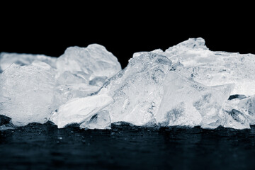 Fototapeta na wymiar Natural ice cubes background. Heap of natural crushed ice on the black reflective surface on black background.