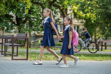 Obraz premium Two schoolgirls go to school with backpacks. Concept back to school, learning, friendship