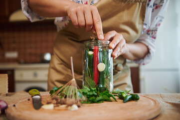 Close-up of a woman, putting peeled fresh garlic in the glass jar with fresh chili peppers, cooking...