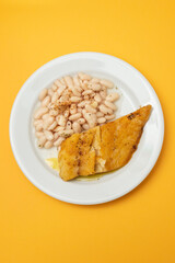 Fried cod fish with white beans on the plate.