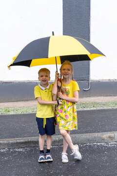 Portrait of two smiling children, a boy and a girl, standing under an umbrella in the park in summer. Children rejoice in the summer rain.