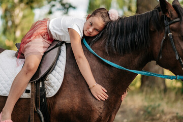 The girl lies on a horse and hugs her. Rehabilitation of a child through contact with a horse.