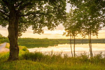 a beautiful blue lake with some tree silhouettes in the foreground under a dramatic sunset sky. High quality photo