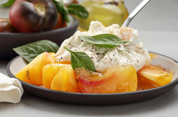 Burrata or mozzarella cheese with yellow-red tomatoes and basil leaves in a plate. Shallow depth of field