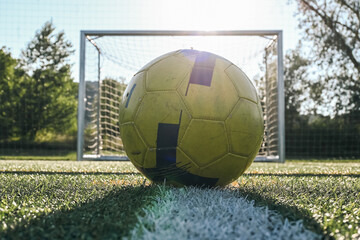 Yellow ball placed on the penalty spot in front of empty goal posts on football training turf at...