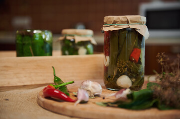 Still life with fermented, salted and marinated foods. A jar of pickled chili peppers on wooden board with fresh ingredients and fragrant culinary herbs. Preparing homemade canned seasonal vegetables