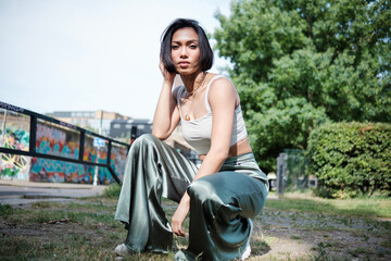 Fashion portrait of young asian female looking at camera, squat.