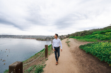 Young Japanese man walking along a path on the cliff by the ocean in business professional clothing
