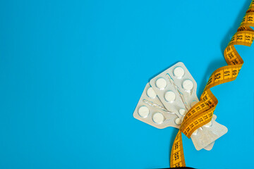 Tablets in plates wrapped with centimeter tape on a blue background. the plates are narrowed in middle, forming a waist or hourglass. concept of weight loss, fat burner, vitamins, sports nutrition. - obrazy, fototapety, plakaty