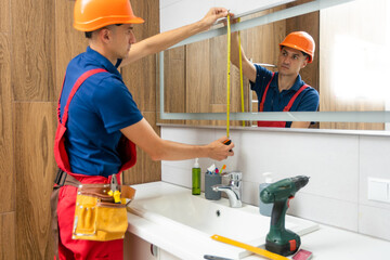 The worker installs the mirror in the bathroom.