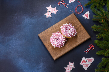 Pink glazed doughnut and marshmallow with Christmas decorations on a wooden cutting board