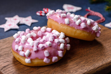 Pink glazed doughnut and marshmallow with Christmas decorations on a wooden cutting board