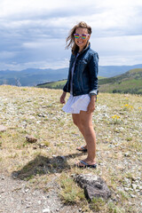 Naklejka na ściany i meble Cute woman tourist wearing a jean jacket poses at the Mt. Washburn overlook in Yellowstone National Park, hair blowing in the wind