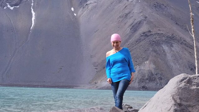 Adult hispanic woman with cancer walks happily on the shore of a lake in the mountains.