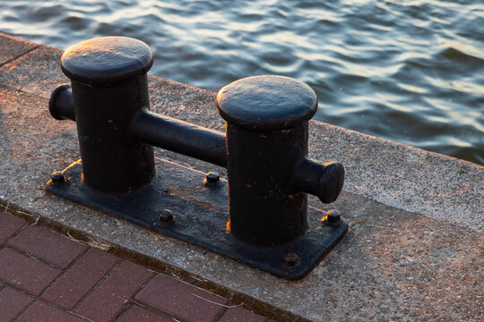 Black coastal bollard is on a concrrete pier, close up