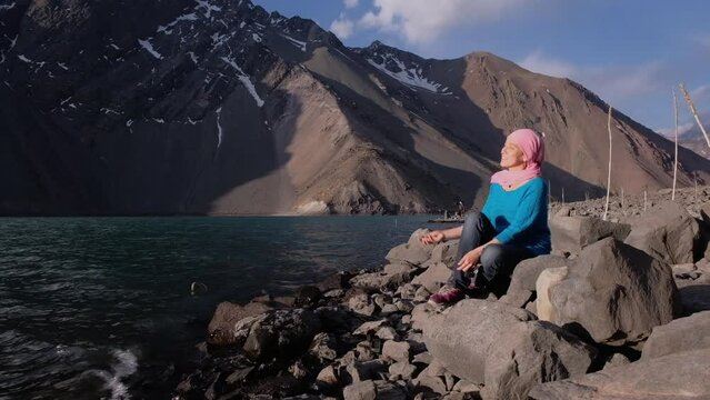 young adult woman in pink scarf throws stones into the water while enjoying the afternoon.